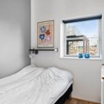 Schlafzimmer mit Bett, Fenster und Wandbild. Auf dem Fensterbrett stehen blaue Vasen.
