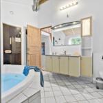 Badezimmer mit Whirlpool, Waschbecken und Toilette. Holztür und Glaswand sichtbar.
