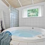 Whirlpool-Bad mit Glasblockwand und Fenster zur grünen Umgebung.