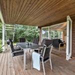 Terrasse mit Esstisch, Stühlen und Grill. Durchgehendes Holzgestühl und -decke.