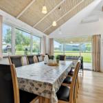 Esszimmer mit langem Tisch und Stühlen, großflächige Fenster und Holzdecke.