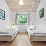 Zwei Einzelbetten in einem hellen Raum mit Holzboden und Fenster. Deckenbalken und Bilder an den Wänden.