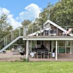 Haus mit Terrasse, Grill und Außensitzgelegenheiten in grüner Umgebung.