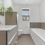 Badezimmer mit Badewanne, Waschbecken und Toilette. Fenster mit Bildern darüber.