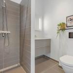 Badezimmer mit Dusche, Waschbecken und Toilette. Wandbild und Pflanze an der Wand.
