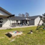 Haus mit Terrasse, Grill, Spielplatz und Hund auf dem Rasen.