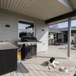 Terrasse mit Grill, Waschbecken und Hund. Liegestühle und Tisch unter Sonnenschutz.