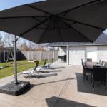 Großer Gartenbereich mit Sonnenschirm, Sitzgruppe und Spielplatz.