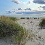 Strand mit Dünen gras und Meer unter blauem Himmel mit Wolken