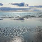 Strand mit feuchtem Sand und Wellen unter bewölktem Himmel