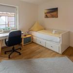 Schlafzimmer mit Bett, Schreibtisch und Fenster. Spiegel und Wandbild sichtbar.