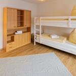 Zimmer mit Doppelstockbett, Holzschrank und Stehlampe auf Holzboden.