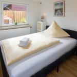 Schlafzimmer mit Bett, Nachttisch und Fensterblick auf Garten.