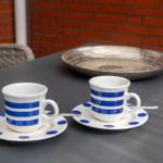 Zwei Tassen mit blauen Streifen stehen auf Untertassen auf einem Tisch.