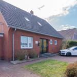 Rotes Backsteingebäude mit Garage und gepflasterter Hof. Ein Auto steht vor dem Haus.