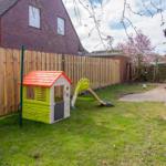 Hinterhof mit Spielhaus und Rutsche, umzäunt und grün.