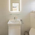 Badezimmer mit Waschbecken, Spiegel, Dusche und Toilette.