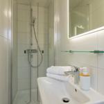 Badezimmer mit Dusche, Waschbecken und beleuchtetem Spiegel.