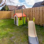 Hinterhof mit Spielhaus und Rutsche, umzäunt mit Holzzaun.