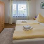 Schlafzimmer mit Doppelbett, Kleiderschrank und Fenster mit Vorhängen.