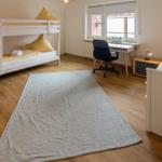 Zimmer mit Doppelstockbett, Einzelbett, Schreibtisch und Fenster.