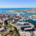 Aerial view of a harbor town with wind turbines, boats, and buildings near the sea.