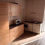 Küche mit Holzschränken, Mikrowelle und Waschmaschine. Tür führt auf Balkon.