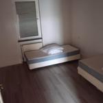 Zwei Einzelbetten in einem Raum mit Holzboden und Fenster mit Jalousie.