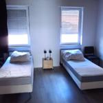 Zwei Einzelbetten, zwei Fenster, Nachttisch mit Lampen, Holzboden.