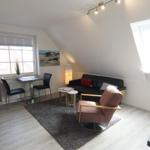 Wohnraum mit Sofa, Sessel, Tisch und Fenstern.