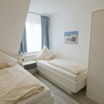 Zwei Einzelbetten, Fenster, Kleiderschrank und Wandbild in einem Zimmer.