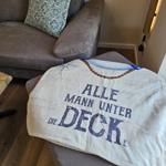 Ein grauer Sofa mit Kissen und ein Decke mit Aufschrift.