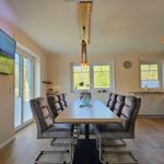 Esszimmer mit langem Tisch, sechs Stühlen und Küchenbereich im Hintergrund.