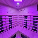Sauna mit Holzwänden und lila Beleuchtung. An den Wänden sind Heizkörper angebracht.
