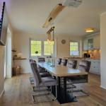 Essbereich mit langer Tisch und Stühlen, Küchenbereich im Hintergrund.