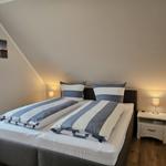 Schlafzimmer mit Doppelbett, Nachttisch und Stehlampe unter schräger Decke.