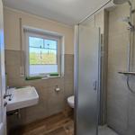 Bad mit Dusche, Waschbecken und Toilette. Fenster mit Blick auf Wald.