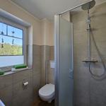Badezimmer mit Dusche, Toilette und Fenster mit Blick auf Wald.