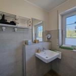 Badezimmer mit Waschbecken, Spiegel und Fenster mit Blick auf Grünfläche.