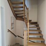 Holztreppe mit Geländer führt zur oberen Etage. Wandbild und Lichtschalter sichtbar.