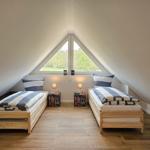 Zwei Betten unter einem Dachfenster mit Blick auf einen Wald.