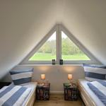 Zwei Betten unter einem Dachfenster mit Blick auf einen grünen Garten.