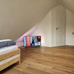 Schlafzimmer mit Dachschrägen, Holzboden und Fernseher.