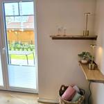 Eingangsbereich mit Holzregalen, Lampe und Korb mit Kissen. Durchgang zur Terrasse mit Garten.
