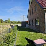 Hinterhof mit Liegestuhl, Grasfläche und Backsteinhaus unter blauem Himmel.