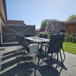 Terrasse mit Tisch und Stühlen neben Haus mit Garten.
