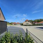Haus mit rotem Dach, gepflasterter Weg und Grünflächen unter blauem Himmel.