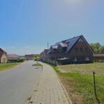 Straße mit Häusern und Grünflächen unter blauem Himmel.