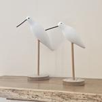 Zwei weiße Vogel-Dekorationsobjekte auf einem Holzregal.
