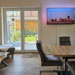 Wohn- und Essbereich mit Fernseher, Sitzgelegenheiten und Blick auf Garten.